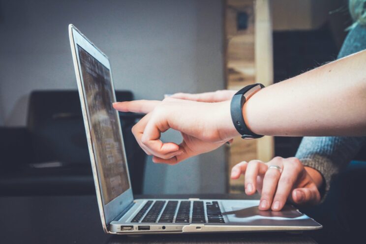 Zwei Hände zeigen auf den Bildschirm eines Laptops.