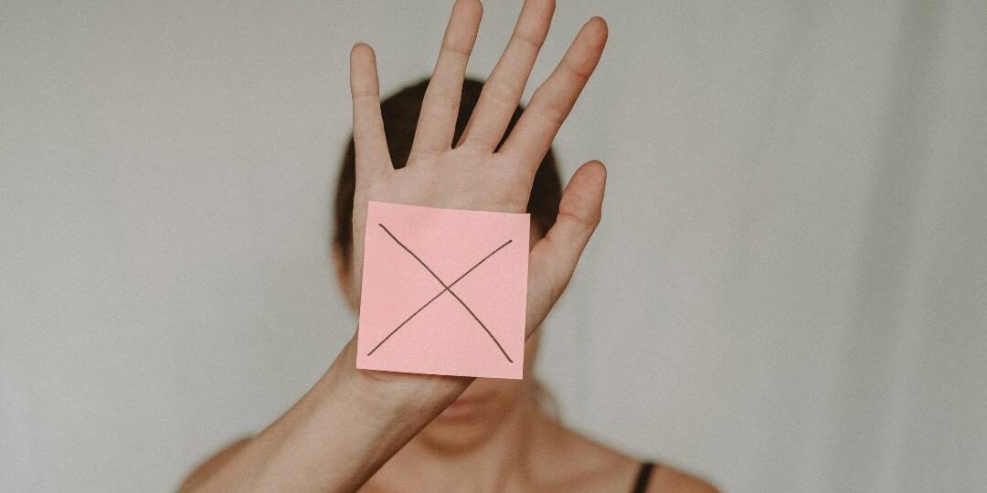 Frau hält rosa Post-it, auf dem ein Kreuz (Nein) zu sehen ist