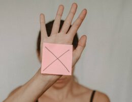 Frau hält rosa Post-it, auf dem ein Kreuz (Nein) zu sehen ist